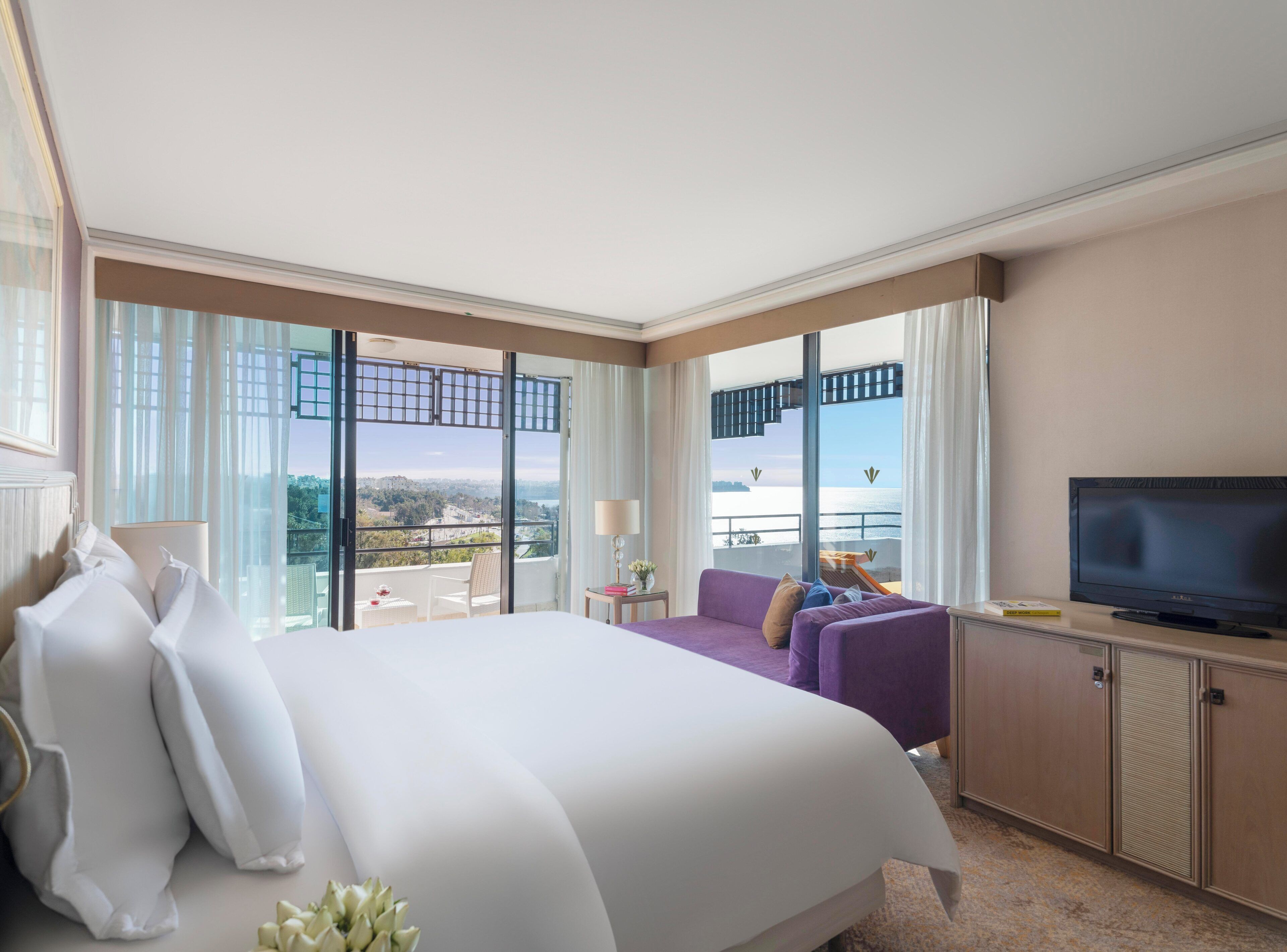 Ein Hotelzimmer mit einem großen Bett, einem Fernseher, einer Couch und einem Balkon mit Meerblick.