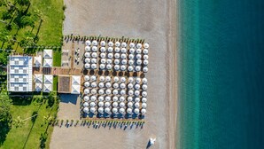 Vista aérea de un resort frente al mar, con hileras de sombrillas y sillas de playa, un edificio de diseño moderno y una vista despejada del océano.