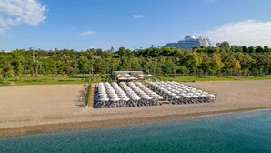 Un complexe hôtelier situé en bord de mer, doté d’une grande piscine, de parasols et offrant une vue sur un hôtel moderne en arrière-plan.