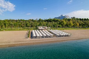 Um resort à beira-mar com uma extensa área de piscina, guarda-sóis e vista para um hotel moderno ao fundo.