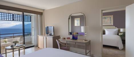 A hotel room with a bed, a desk with a laptop, a chair, a small table with a vase, a lamp, and a large mirror.