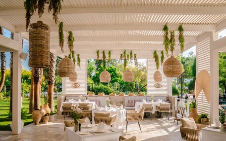 An outdoor dining area with wicker hanging lamps, cushioned seating, and potted plants.