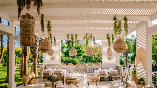 Un espace de restauration en plein air agrémenté de lampes suspendues en osier, de sièges rembourrés et de plantes en pot.