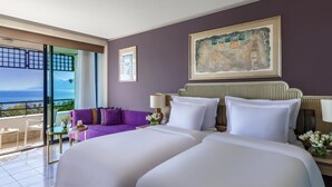 Une chambre d’hôtel avec un grand lit, un canapé violet, une vue sur la mer et un tableau au mur.