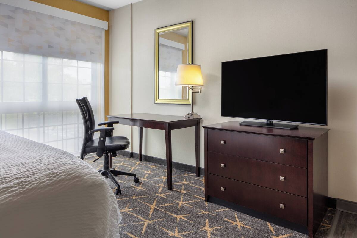 A hotel room with a bed, a desk with a lamp, a TV, and a dresser.