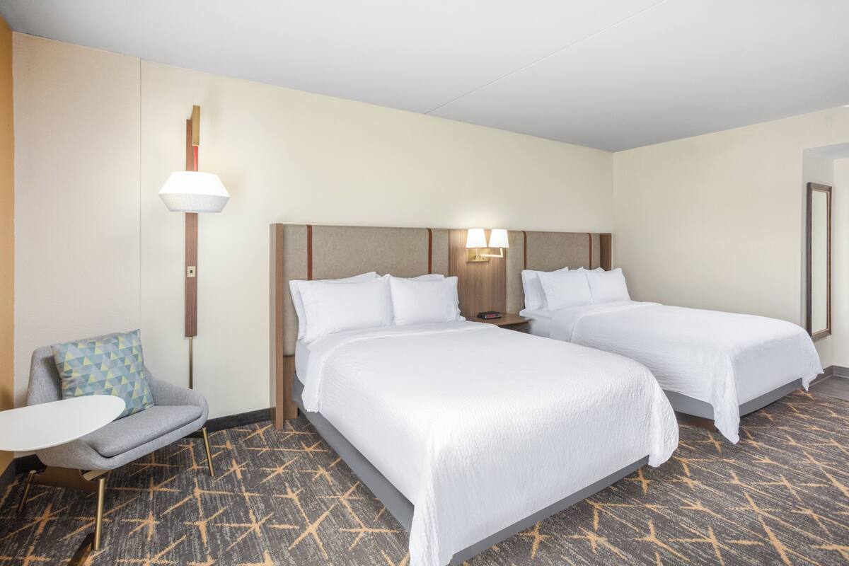 A hotel room with two beds, a small sofa, a table, and a patterned carpet.