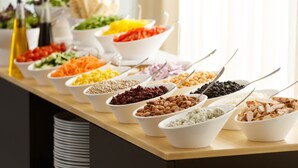 A buffet table with various food items in white bowls, including salads, grains, and legumes.