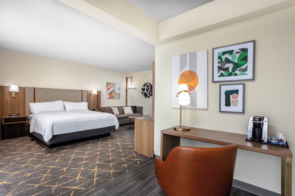 A hotel room with a bed, a desk, a chair, a coffee maker, and artwork on the walls.