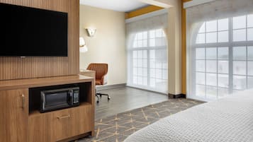 A hotel room with a bed, a television, a microwave, a chair, and large windows.