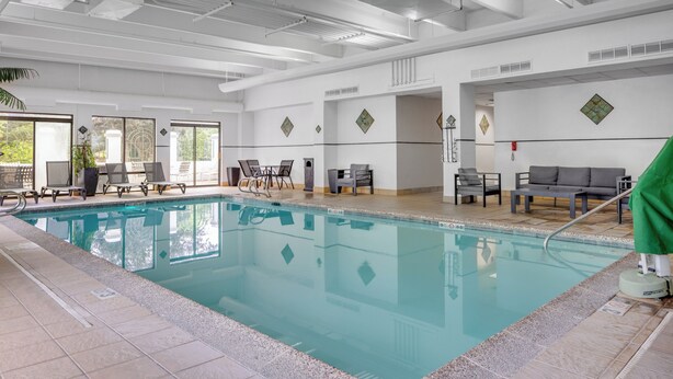 A clean indoor swimming pool with clear water, surrounded by lounge chairs and tables, and a tiled floor.