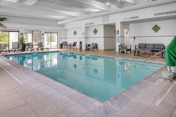 A clean indoor swimming pool with clear water, surrounded by lounge chairs and tables, and a tiled floor.