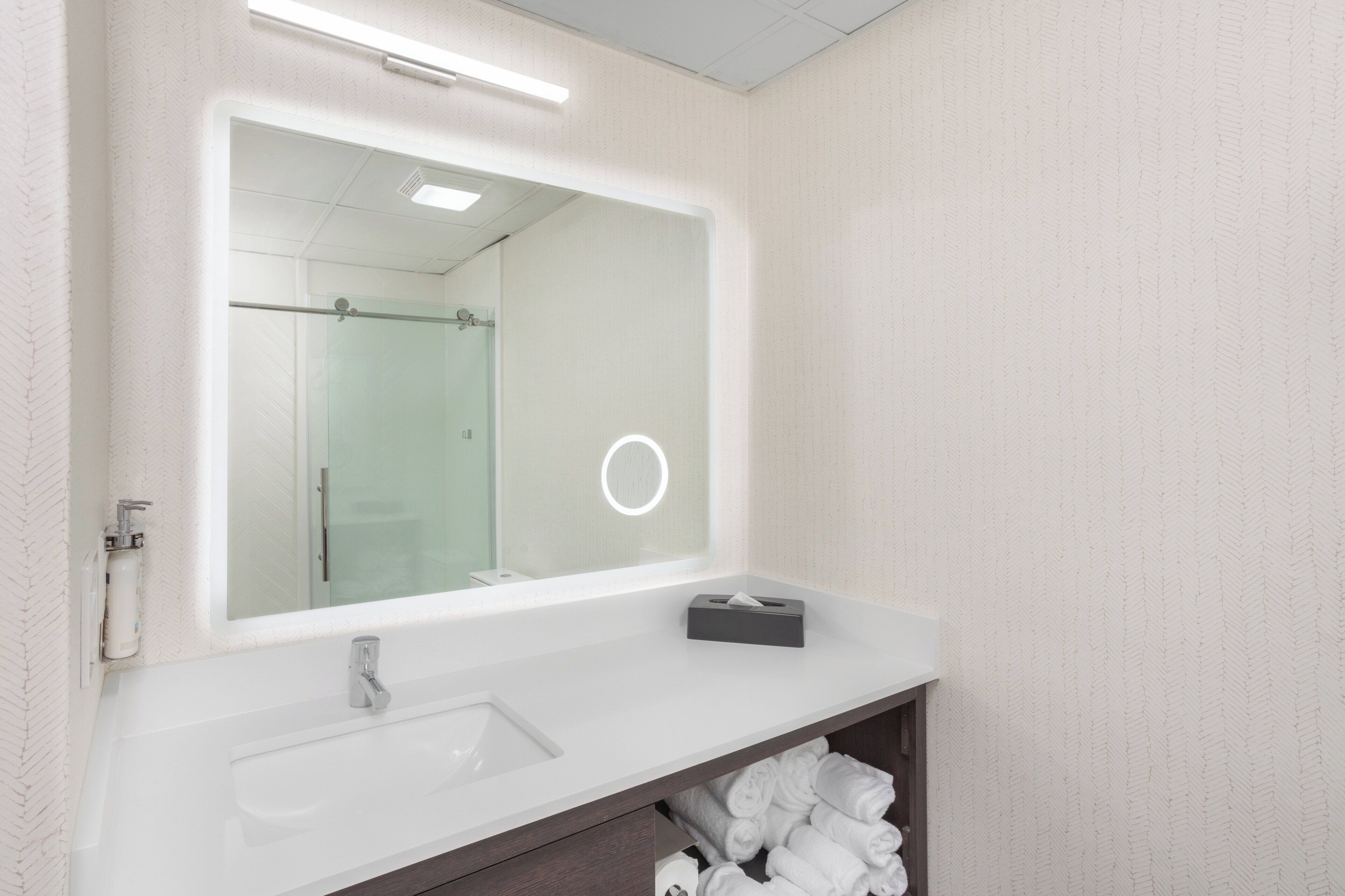A bathroom with a large mirror, a sink, a towel rack, and a toilet.