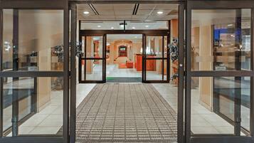 A hotel entrance with automatic sliding doors, a check-in counter, and a carpeted walkway.