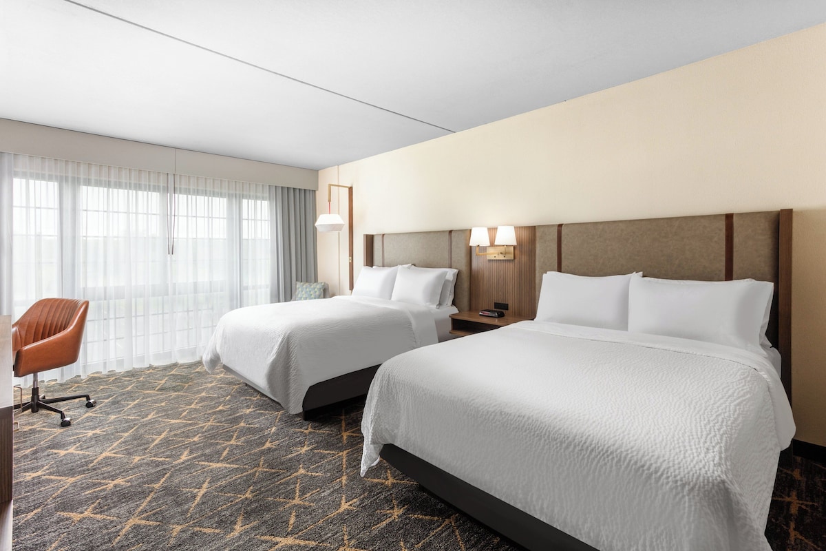 Une chambre d’hôtel avec deux lits, un bureau et une chaise.