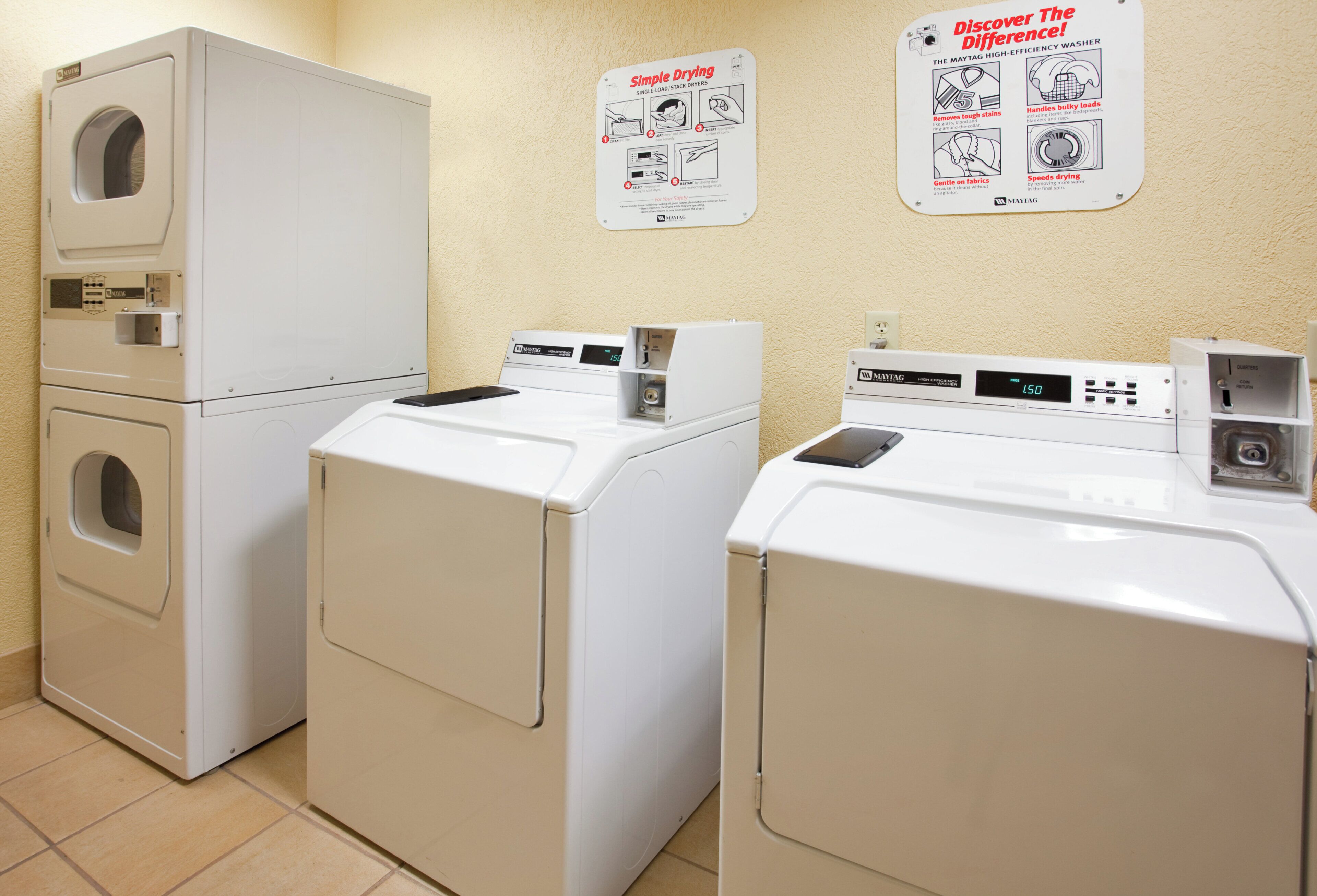 A laundry room with three stacked washers and dryers, a control panel, and instructional posters on the wall.