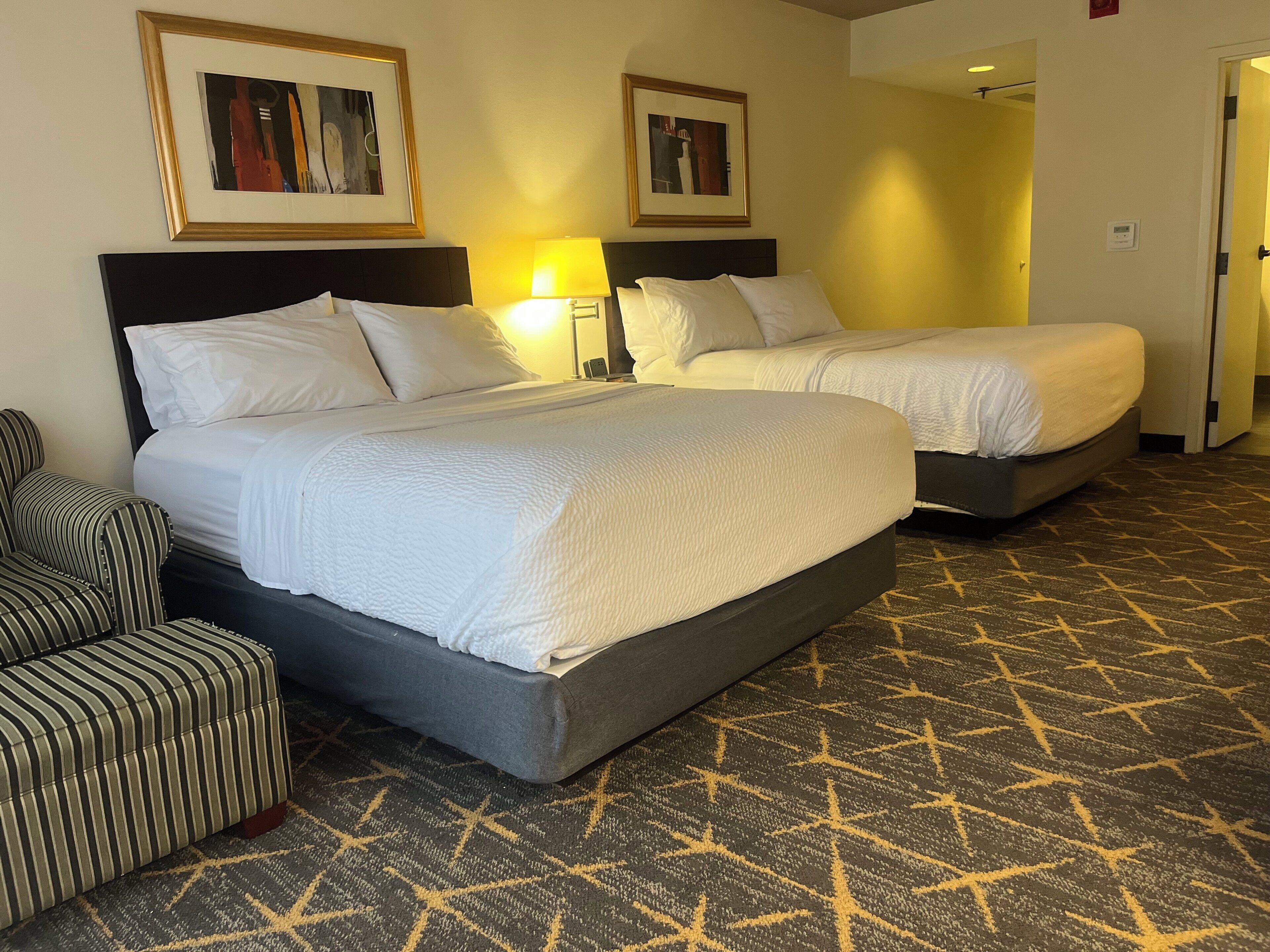 A hotel room with two beds, a striped armchair, and patterned carpet.