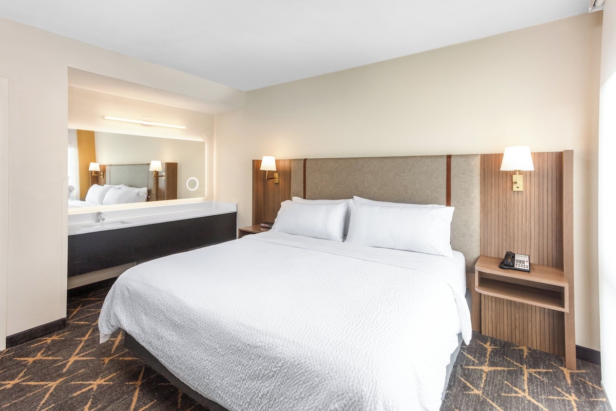 Une chambre d’hôtel avec un grand lit, une salle de bain avec un miroir et une table de chevet avec un téléphone.