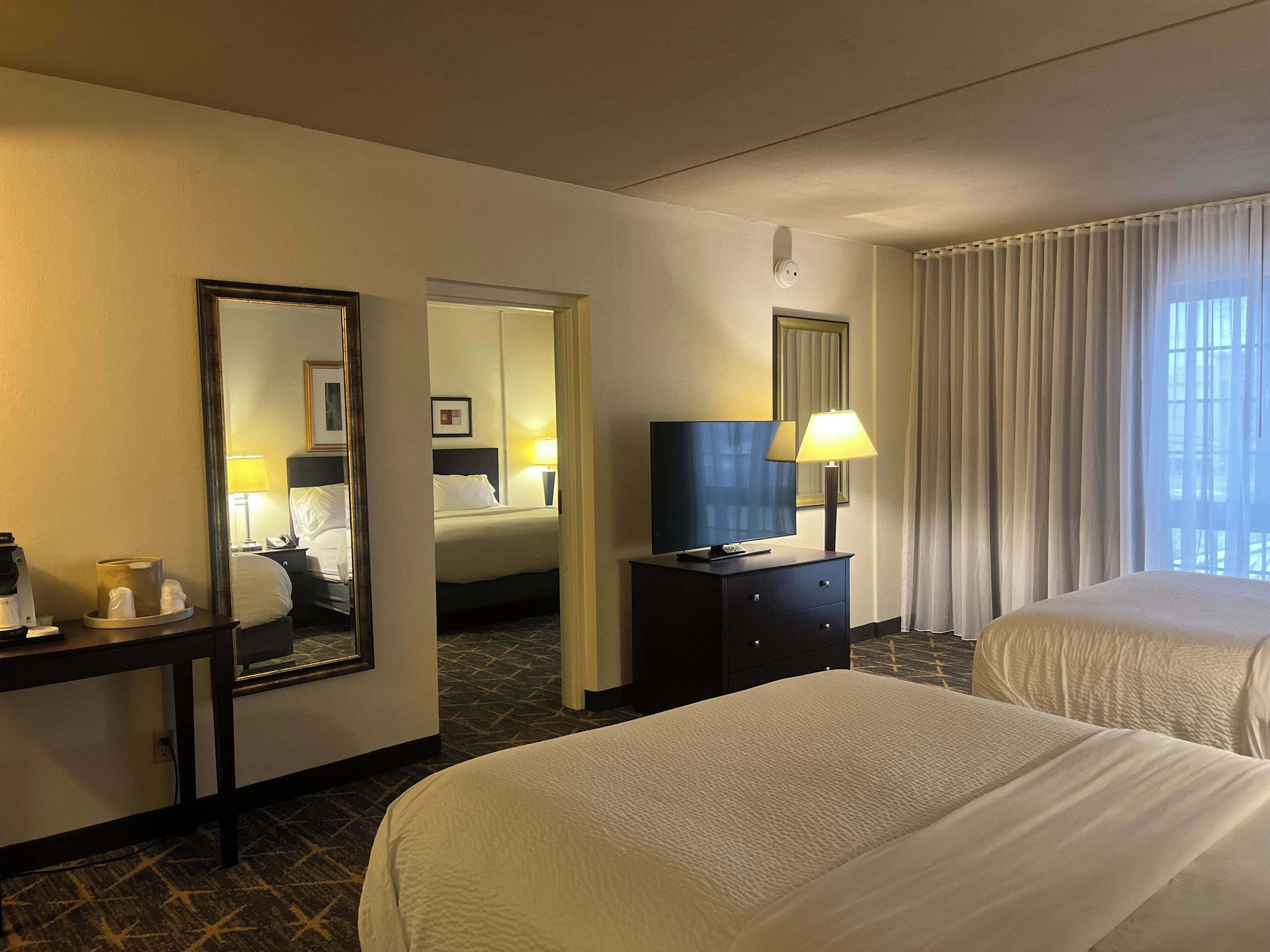 A hotel room with two beds, a television, a desk with a lamp, and a mirror.