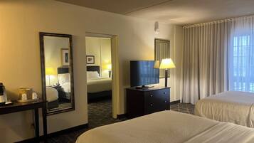 A hotel room with two beds, a television, a desk with a lamp, and a mirror.