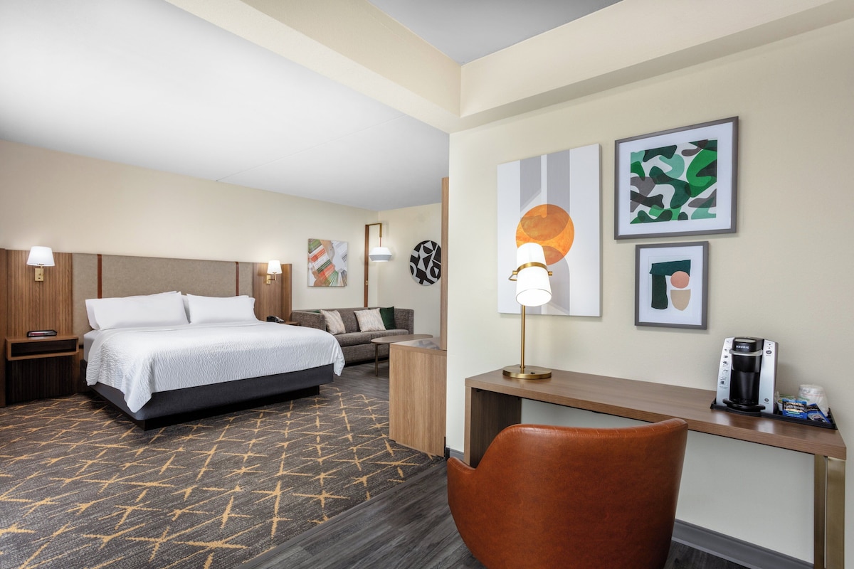 Une chambre d’hôtel équipée d’un lit, d’un bureau, d’une chaise, d’une machine à café et décorée avec des œuvres d’art.