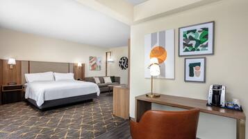 A hotel room with a bed, a desk, a chair, a coffee maker, and artwork on the walls.