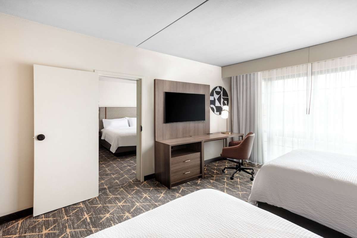Une chambre d’hôtel comprenant un lit, un bureau avec une télévision, une chaise et une porte donnant sur une autre pièce.