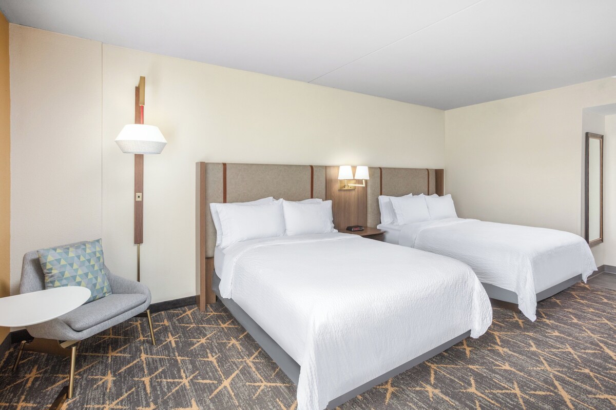 Une chambre d’hôtel avec deux lits, un petit canapé, une table et une moquette à motifs.
