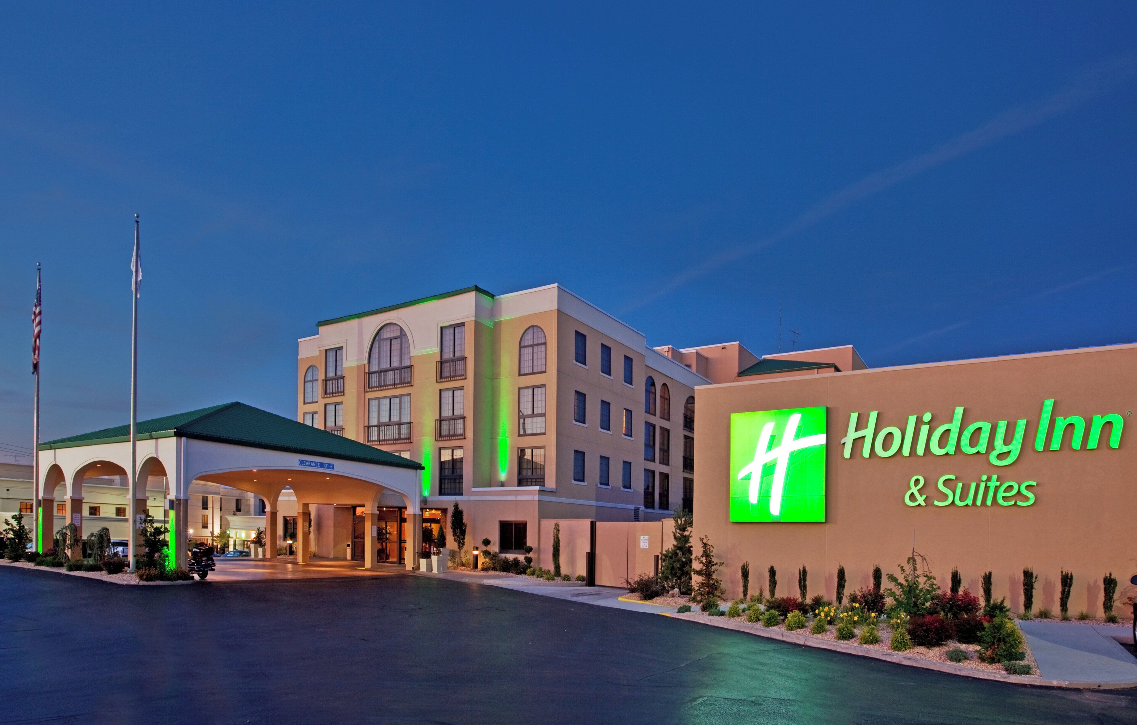 Ein Holiday Inn & Suites Gebäude mit einem gut sichtbaren Eingang, mehreren Stockwerken und einer sichtbaren amerikanischen Flagge.