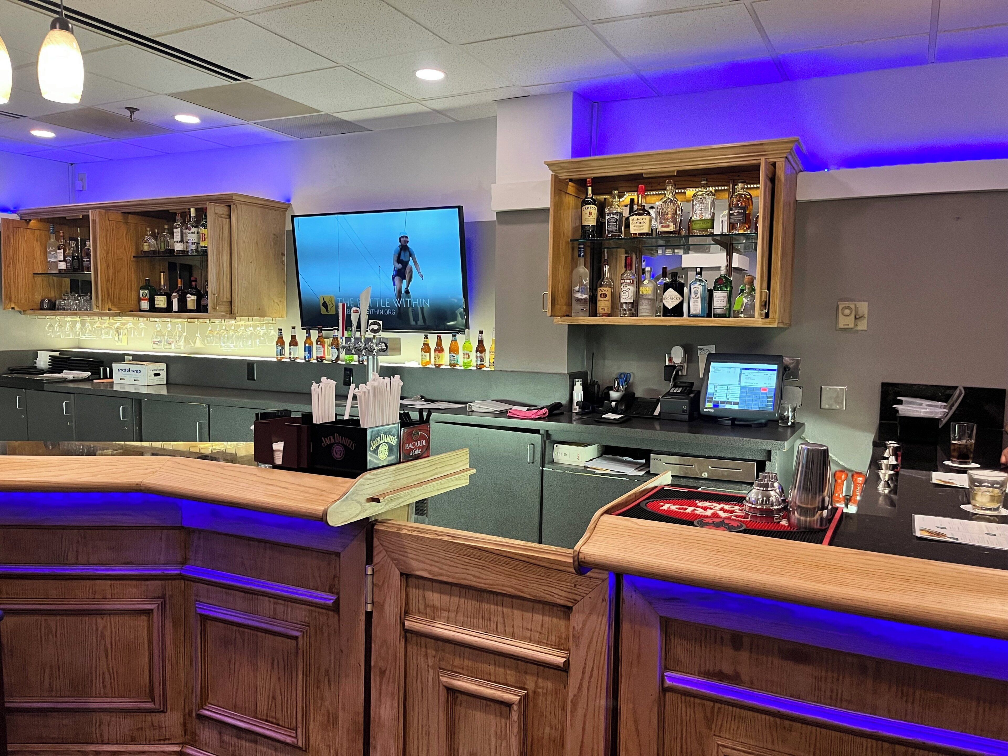 A bar area with wooden cabinets, a television screen, and a variety of liquor bottles.