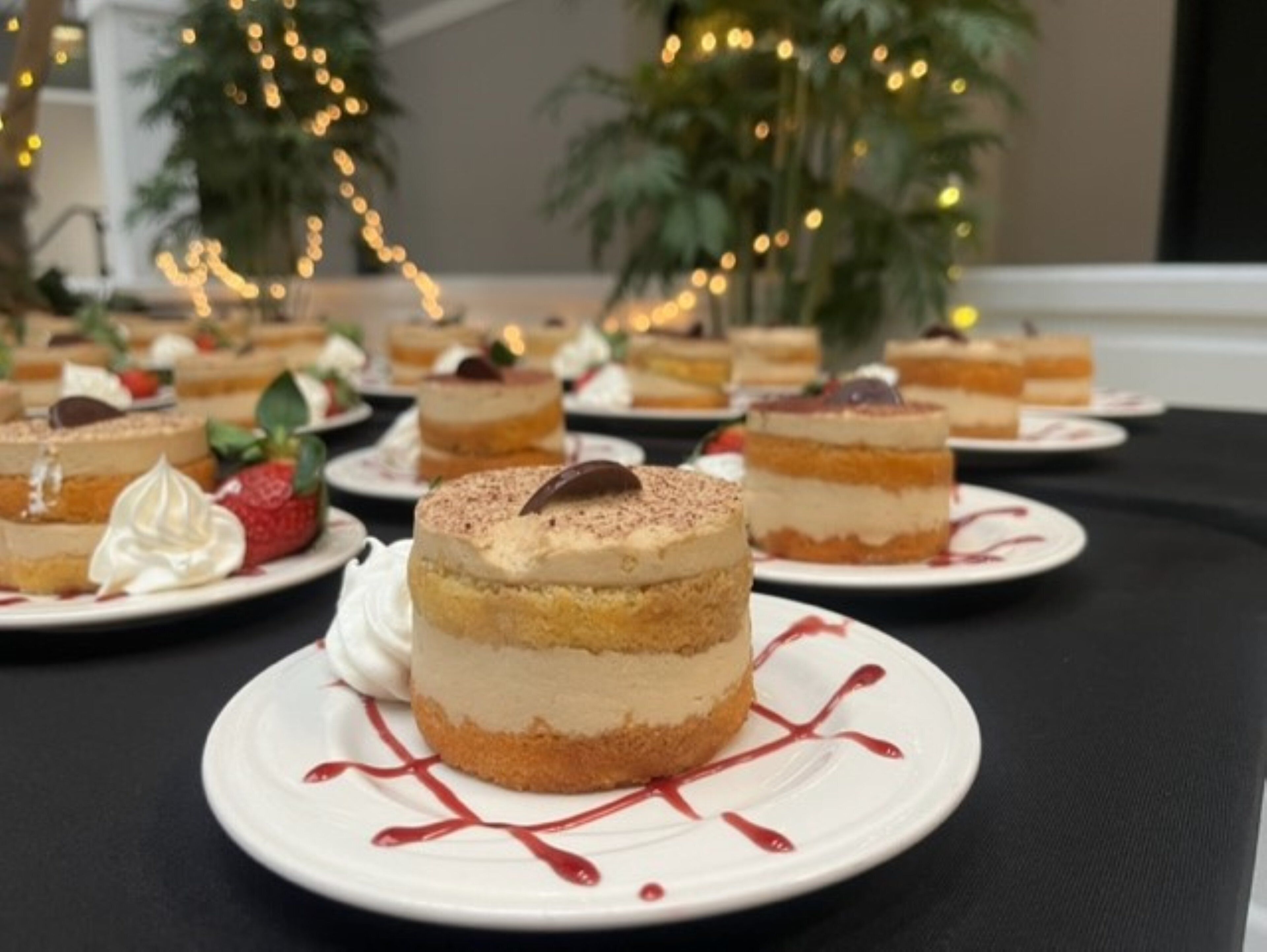 Une table de desserts avec des gâteaux à plusieurs étages et de la crème fouettée, le tout mis en valeur par un décor de verdure et de guirlandes lumineuses.