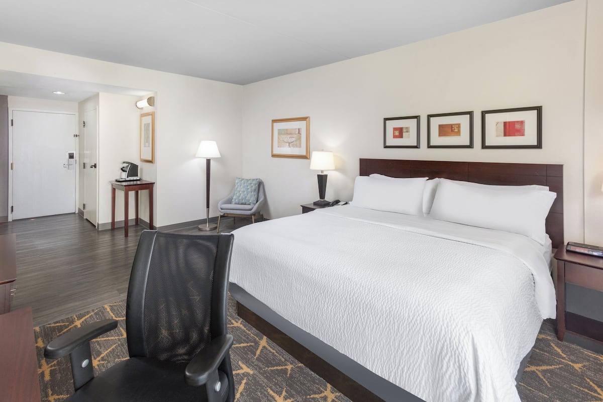 A hotel room with a large bed, a desk, a chair, a lamp, and framed pictures on the wall.