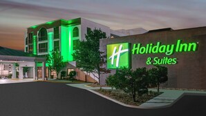A Holiday Inn & Suites building with a prominent illuminated sign, a covered entrance, and a landscaped area with trees.