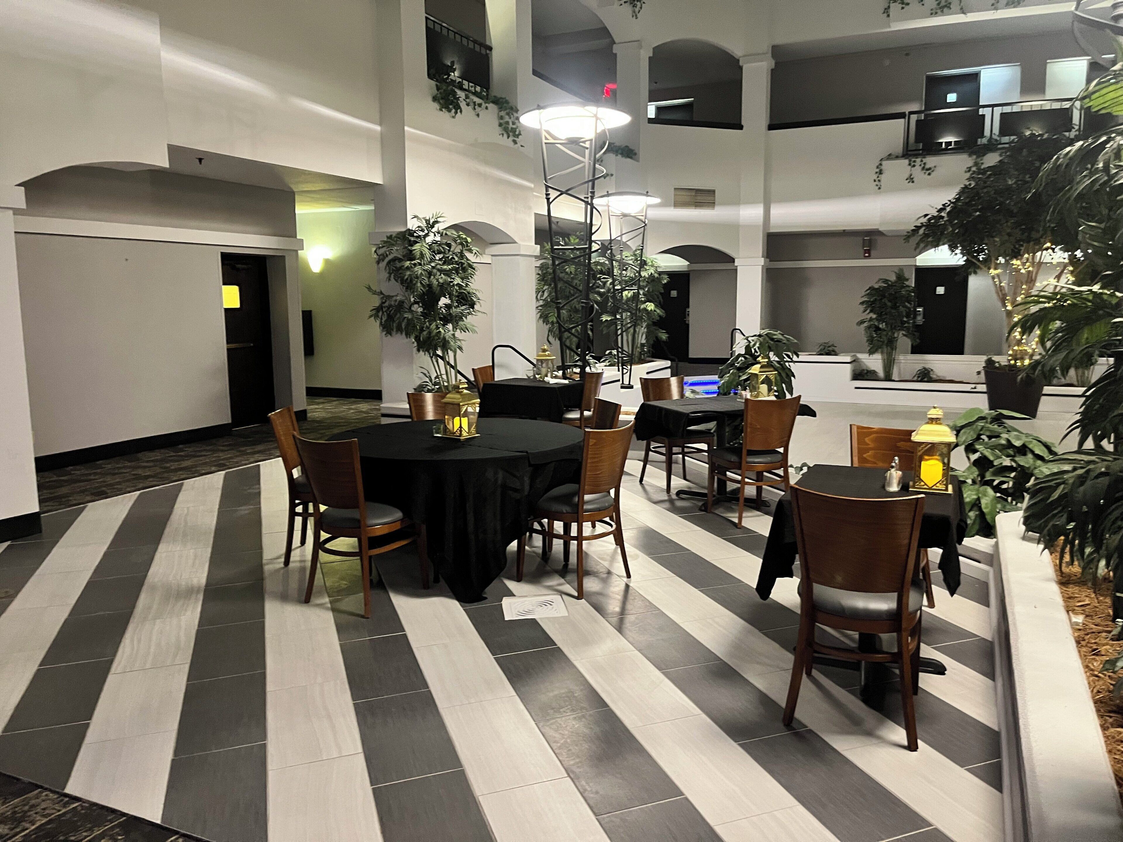 A hotel dining area with round tables, chairs, and potted plants.