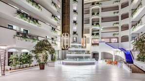 A spacious atrium with a central water feature, multiple balconies with greenery, and a staircase with blue lighting.