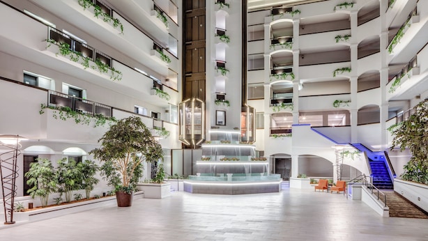 A spacious atrium with a central water feature, multiple balconies with greenery, and a staircase with blue lighting.