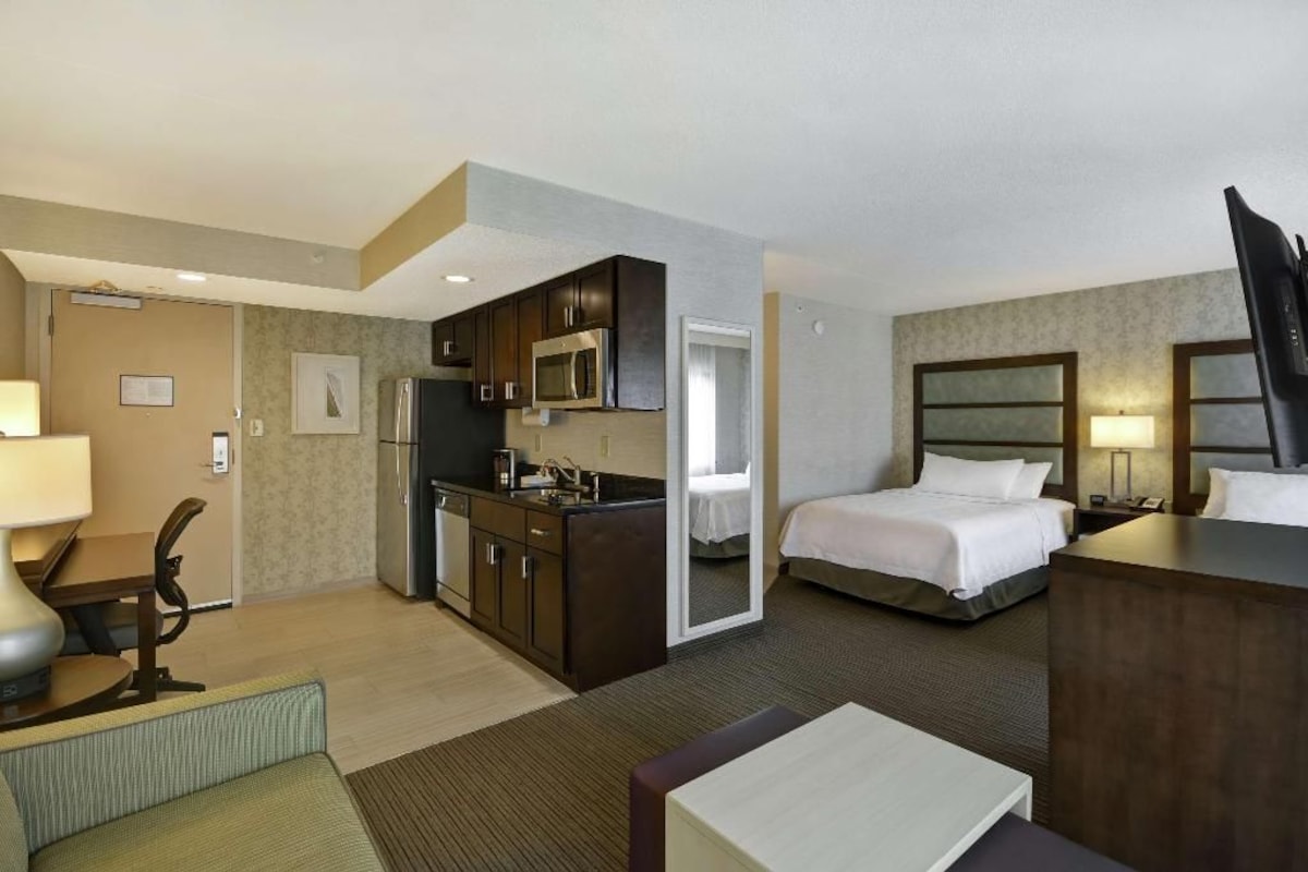 Een hotelkamer met een kitchenette, een bed, een bureau en een stoel.