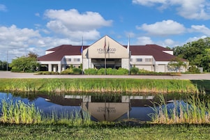 A hotel with a central entrance, a landscaped front yard, and a body of water reflecting the building.
