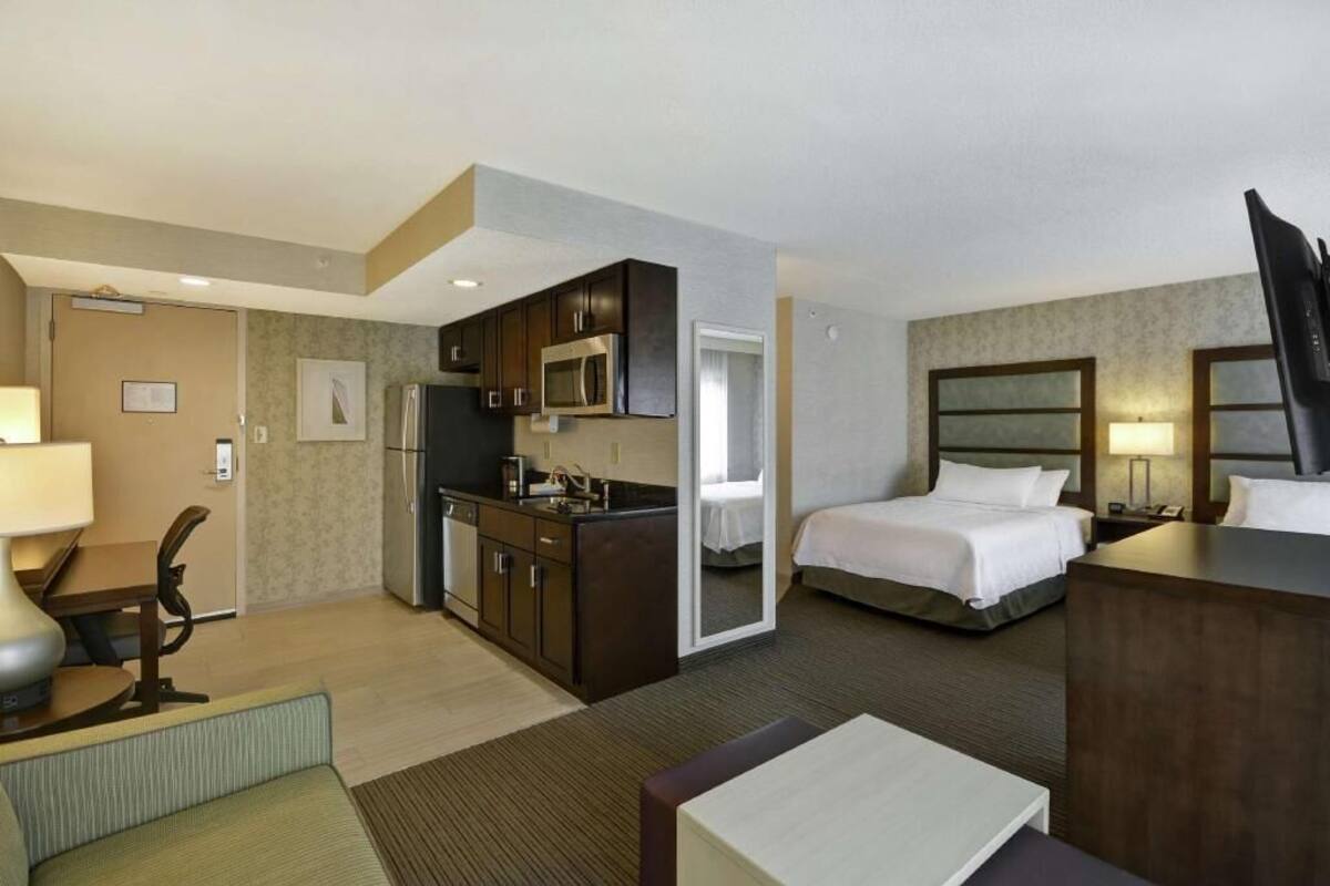 Een hotelkamer met een bed, een bureau, een stoel, een kitchenette en een badkamer.