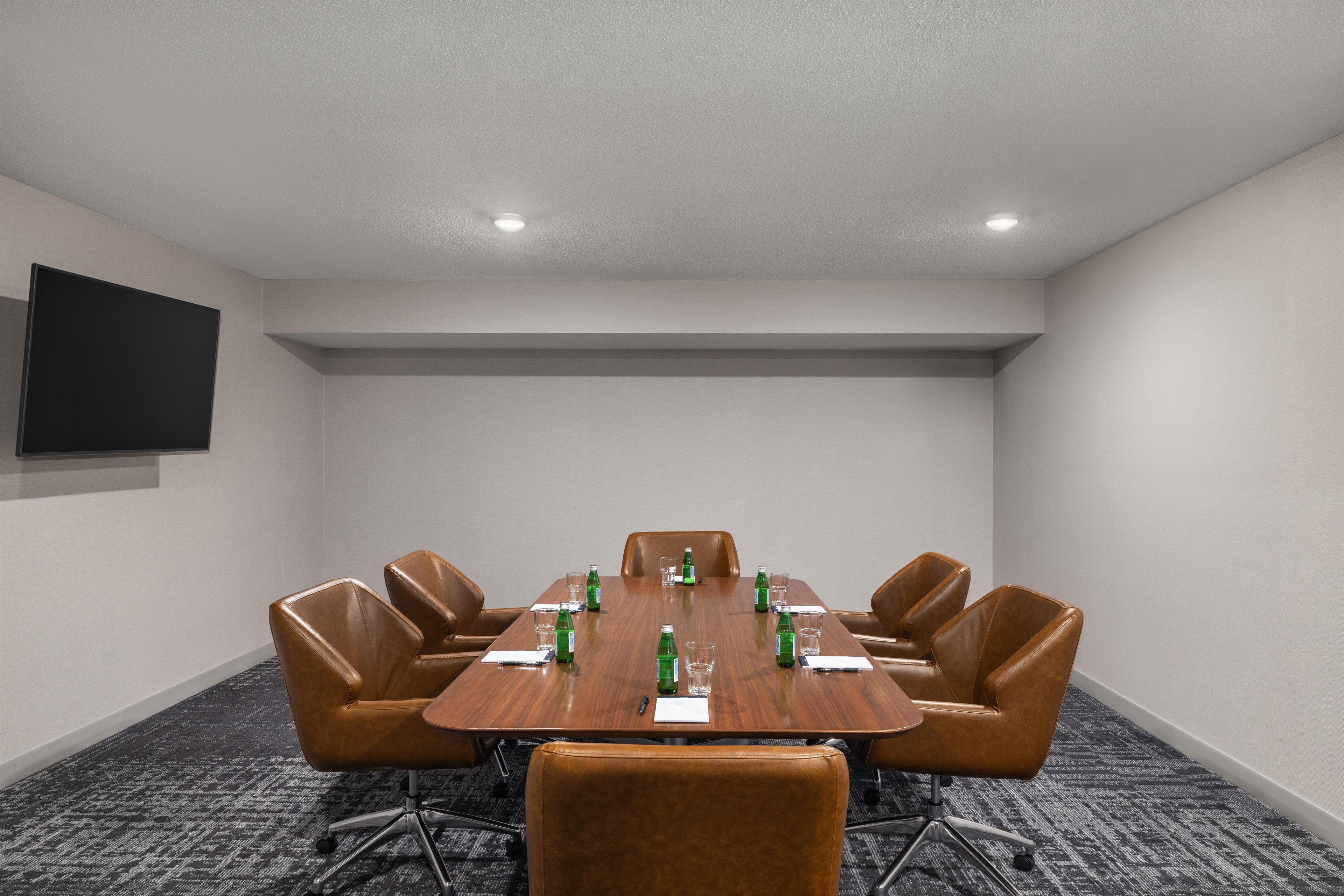 A conference room with a long table, six chairs, and a flat-screen TV on the wall.