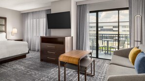 Een hotelkamer met een bed, een bureau, een bank, een televisie en een balkon met uitzicht op de stad.