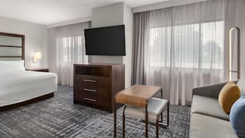 A hotel room with a bed, a TV, a desk, a chair, and a sofa.