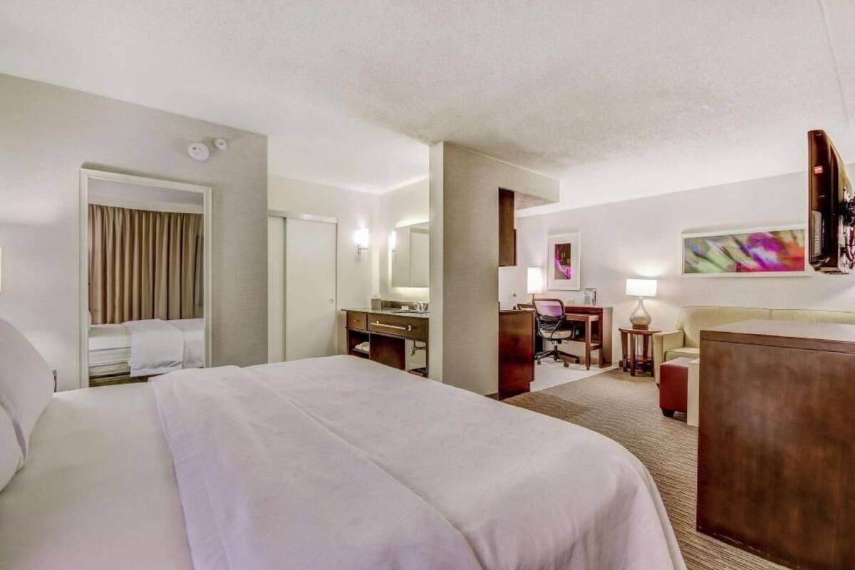 Hotelkamer met een groot bed, een bureau met stoel, een klein tafeltje met lamp en een aan de muur bevestigde televisie.