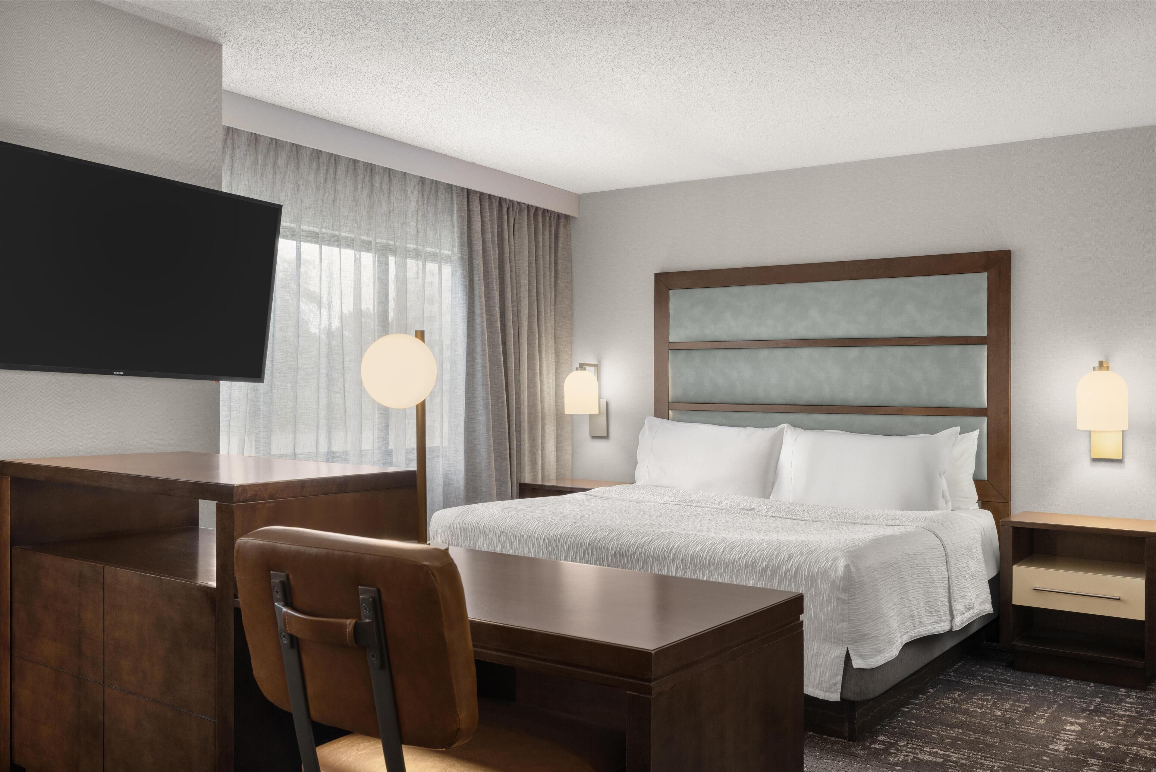Una habitación de hotel con una cama, un escritorio, una silla, un televisor y dos lámparas de noche.