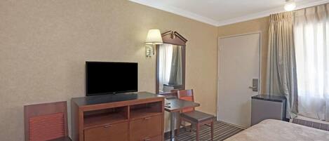 Ett hotellrum med en säng, ett skrivbord med en platt-TV, en spegel, en stol och ett litet bord.