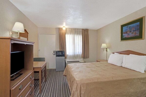 Una habitación de hotel con cama, televisión, escritorio y una pequeña cocina.