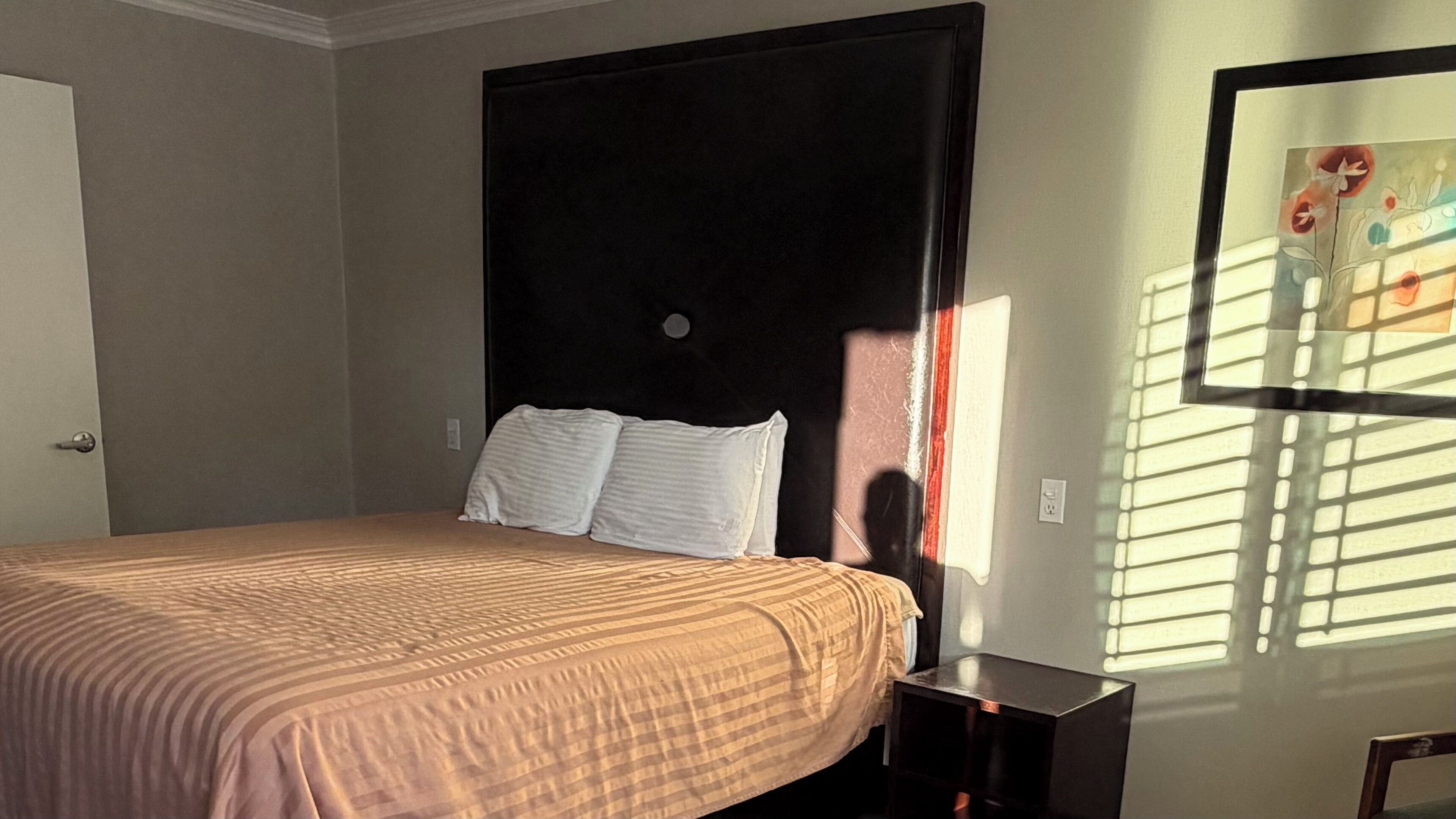 A bedroom with a bed, a nightstand, a wall clock, and a window with blinds.