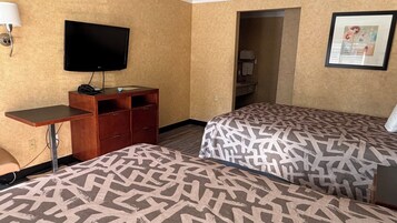 Habitación de hotel con dos camas, un escritorio, un televisor y una puerta que da a un baño.