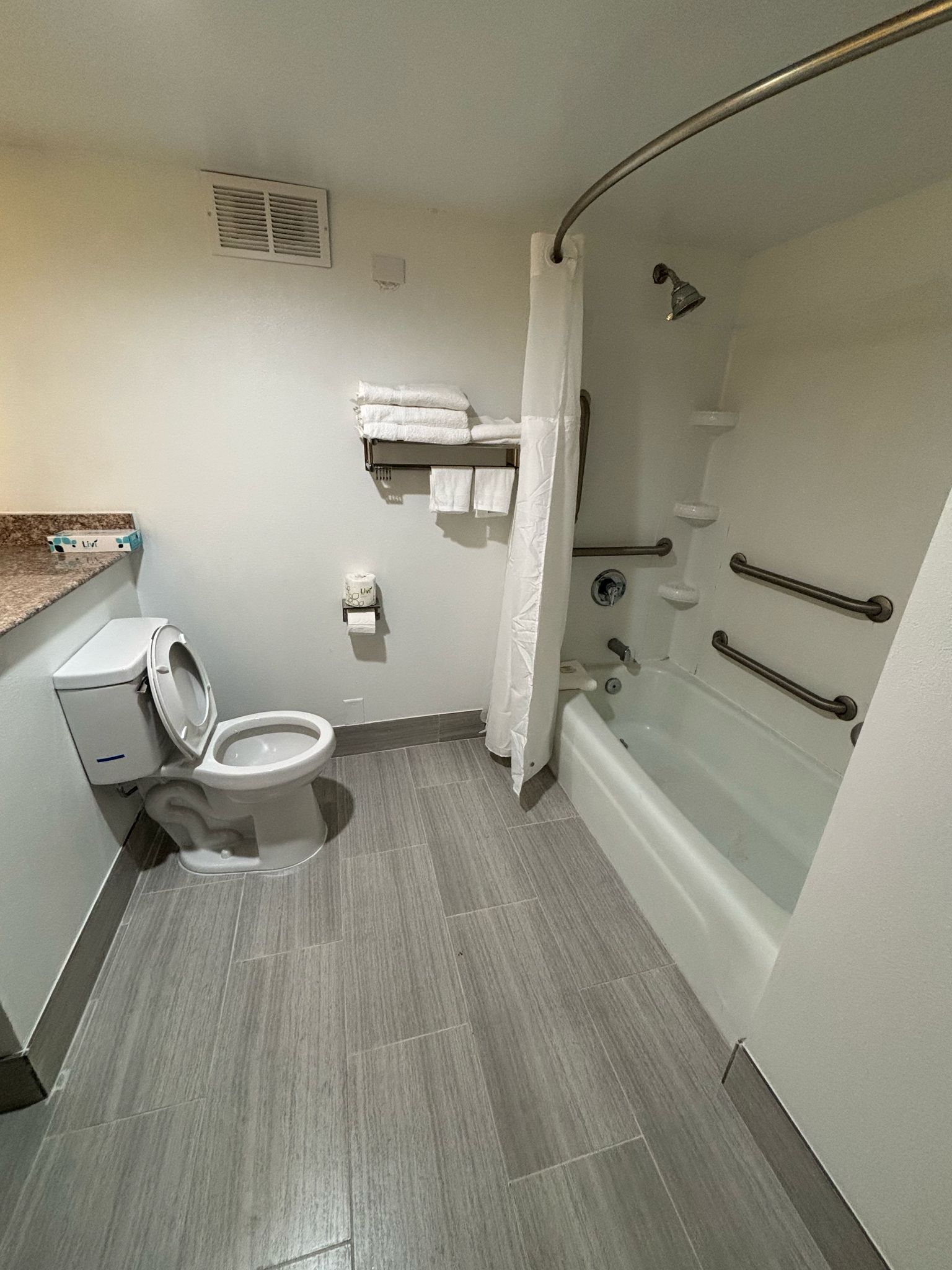 A compact bathroom with a toilet, a bathtub with grab bars, a shower curtain, and a towel rack.