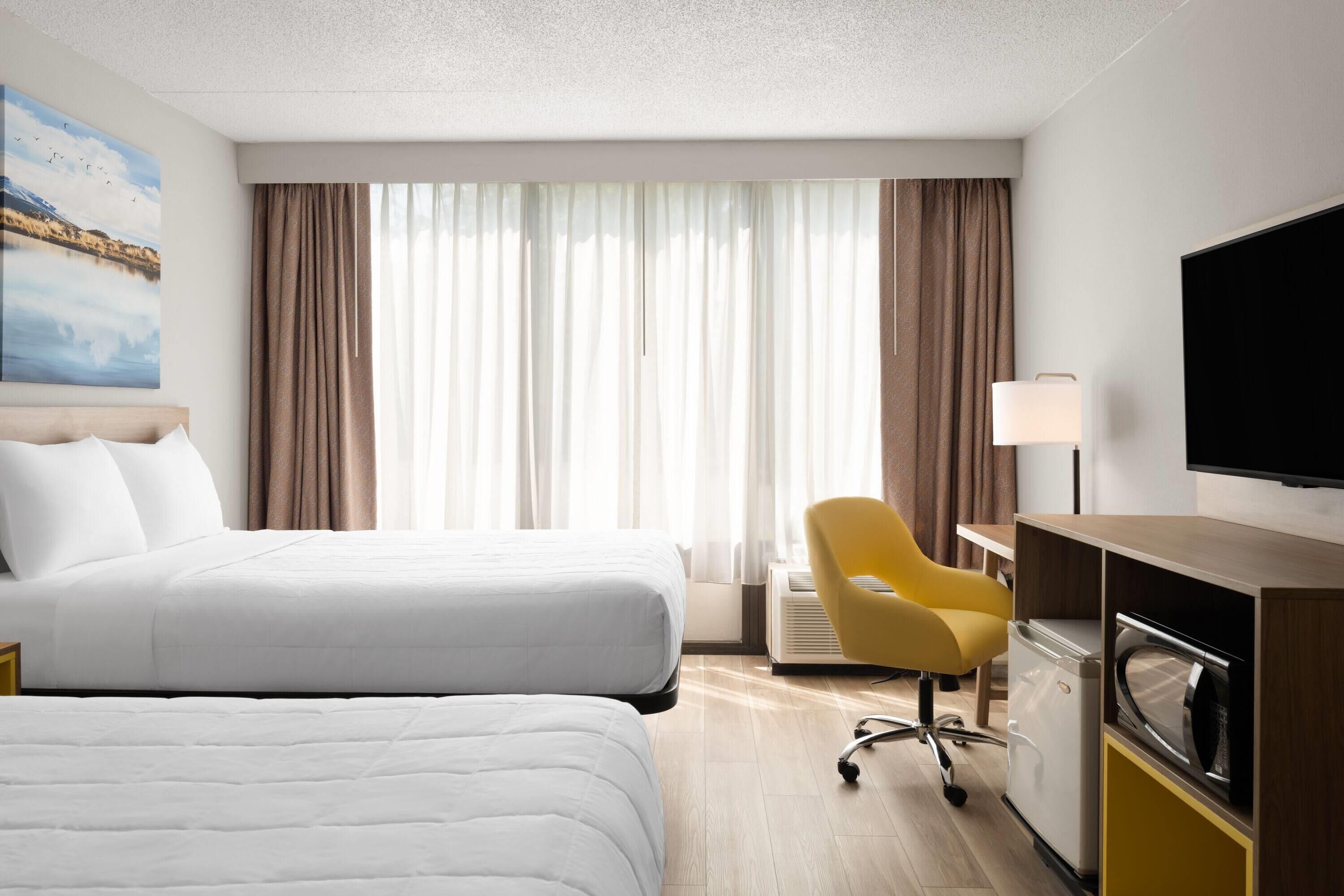 A hotel room with two beds, a TV, a desk, a chair, and a microwave.