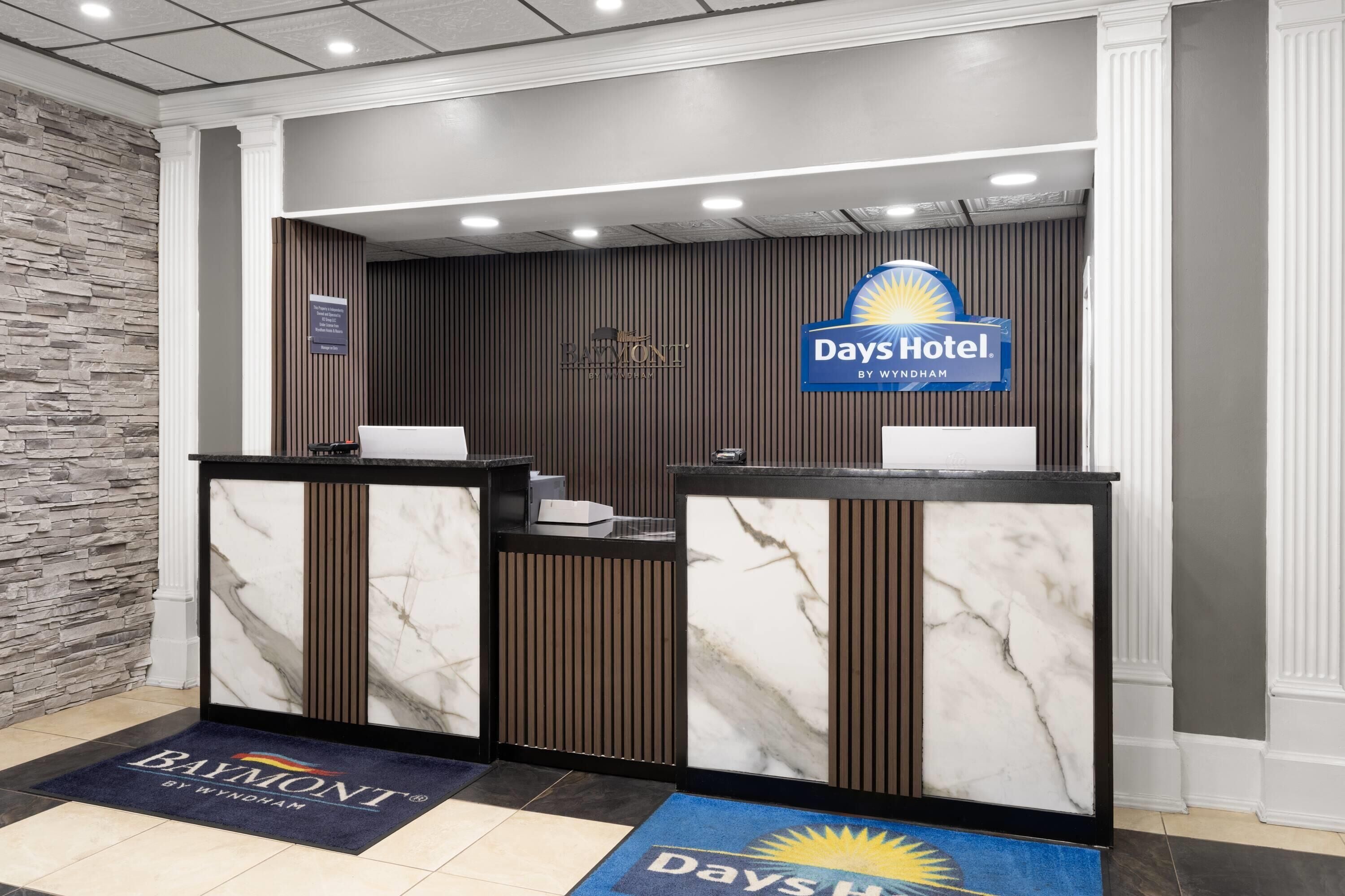 Un'area reception con un bancone in marmo, un cartello Days Hotel e il logo Baymont.